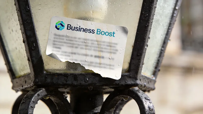 A wet, slightly damaged Business Boost sticker attached to a damp, dark metal vintage street lamp post.
