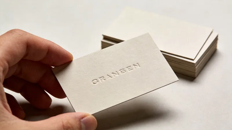 A hand holding a minimalist textured business card with the embossed word GRANSEN printed on it.
